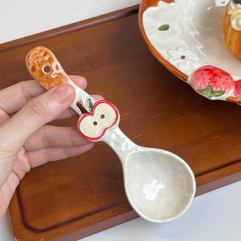 Ceramic spoon with apple design held by a hand on a wooden surface