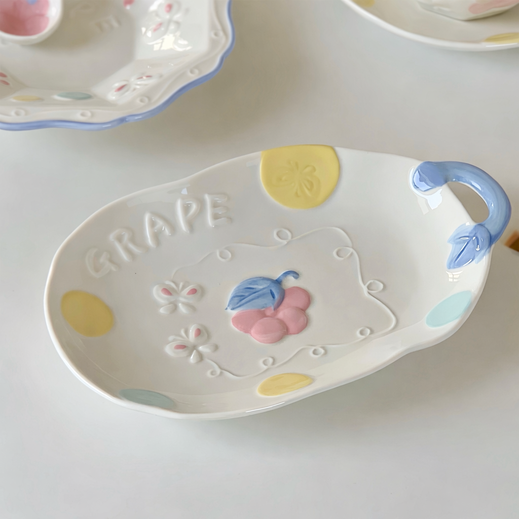 Decorative ceramic plate with cartoon design and 'GRAPE' text on a white surface