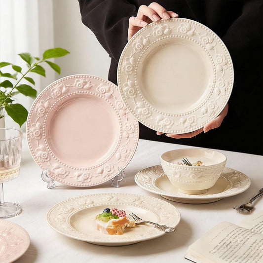 Two 8-inch ceramic plates with embossed floral borders in pastel pink and cream white, featuring a croissant on the pink plate.